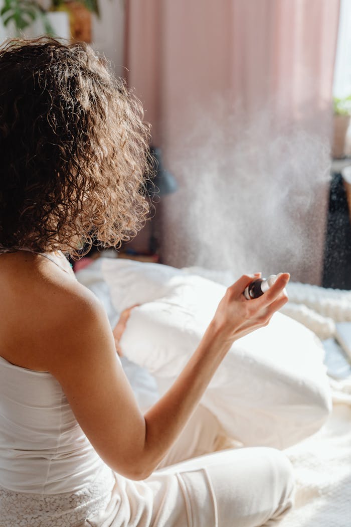 A woman in a cozy indoor setting using an aromatherapy spray on her pillow for relaxation.